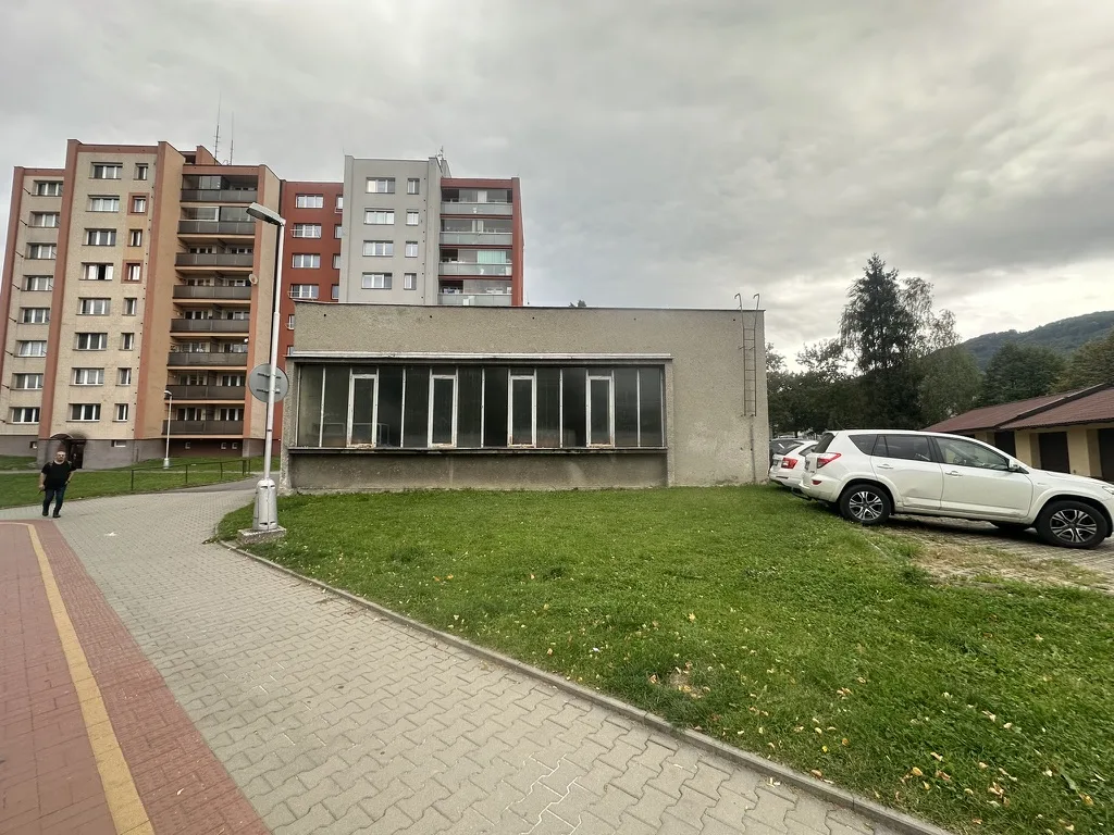 Současný stav: šedá budova bývalého výměníku s okny, tráva a paneláky v pozadí